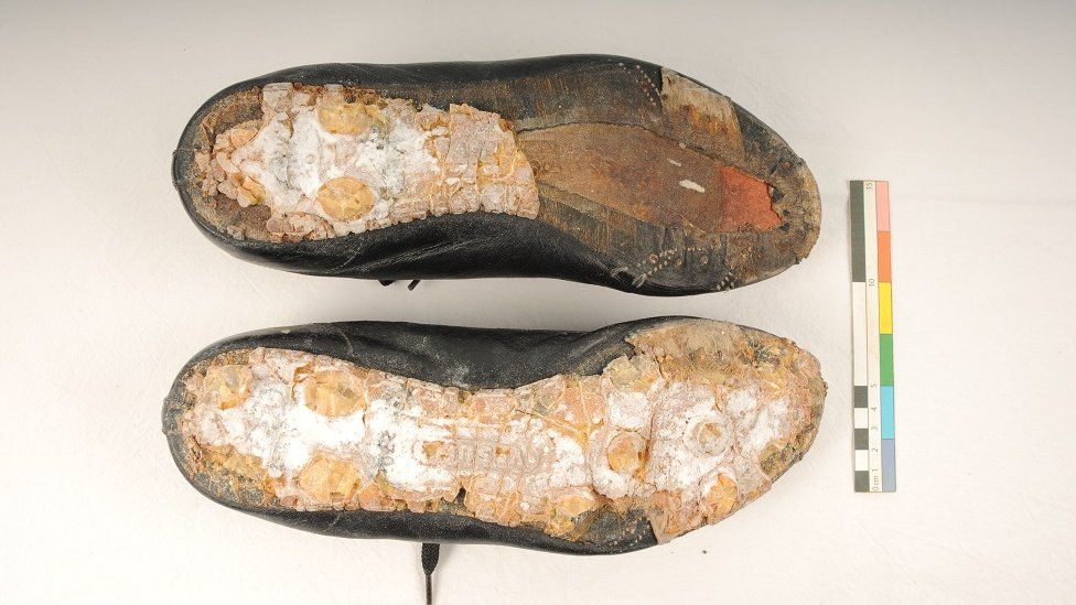 Pair of old football boots upside down, showing hardly any of the soles left, but the leather upper intact