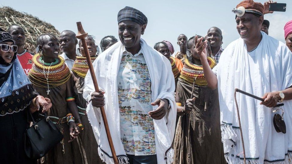 William Ruto (C) and Marsabit County Governor Mohammed Muhamud Ali (R) walk with performers of the Turkana tribe during the 11th Marsabit Lake Turkana Culture Festival in Loiyangalani near Lake Turkana, northern Kenya, on June 28, 2018