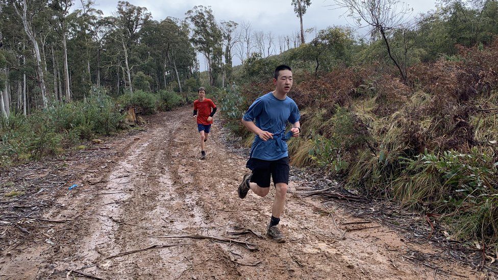 Two students running along a muddy track