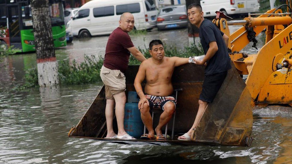 People stand on a front loader travelling through floodwaters after the rains and floods brought by remnants of Typhoon Doksuri, in Zhuozhou, Hebei province, China