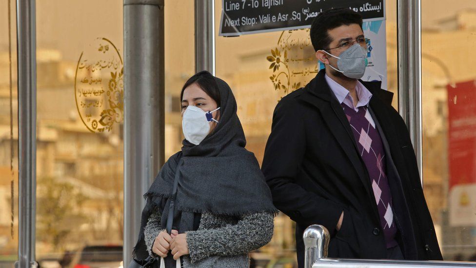 People wearing protective masks stand at a bus station in the Iranian capital Tehran on February 24, 2020