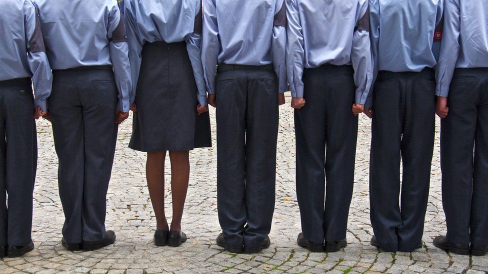 Backs view of tight row of British air force cadets in blue uniforms, standing on square.