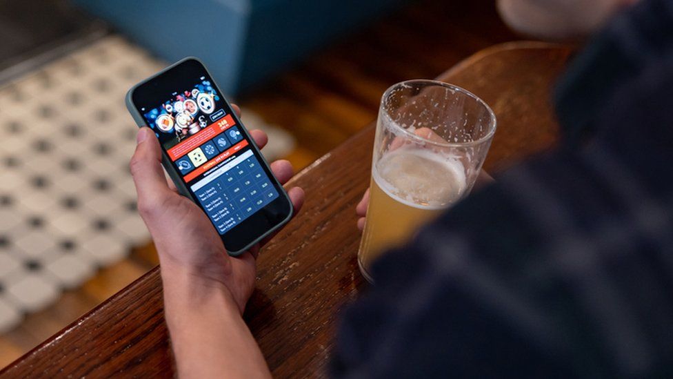 Close-up on a man gambling online using a mobile app on his cell phone while drinking beer at the pub