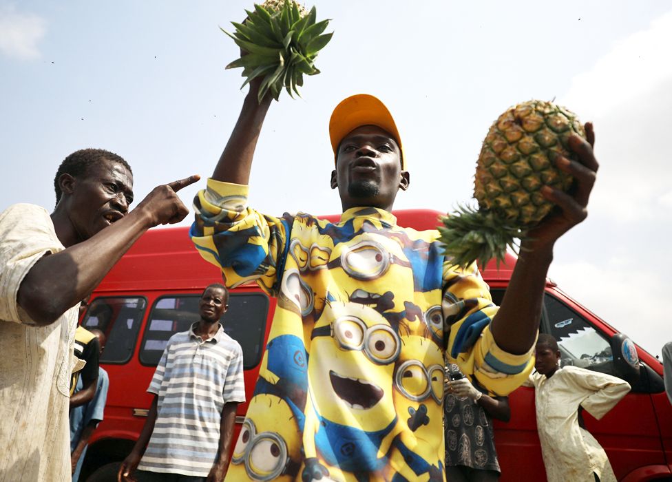 A fruit seller in a Minions shirt holds up pineapples in Abuja, Nigeria - Thursday 9 April 2020