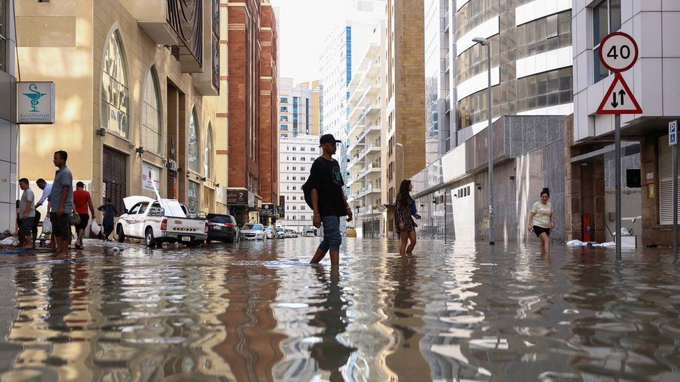 People walk through flood water caused by heavy rains, in Dubai..