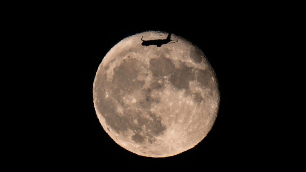 Пассажирский самолет, летящий над полной луной перед посадкой в ​​международном аэропорту Сан-Франциско, сфотографирован из Берлингейма в Калифорния, США, 2 августа 2023 г.