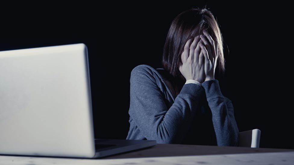 A woman hiding her face in dismay while looking at her computer.