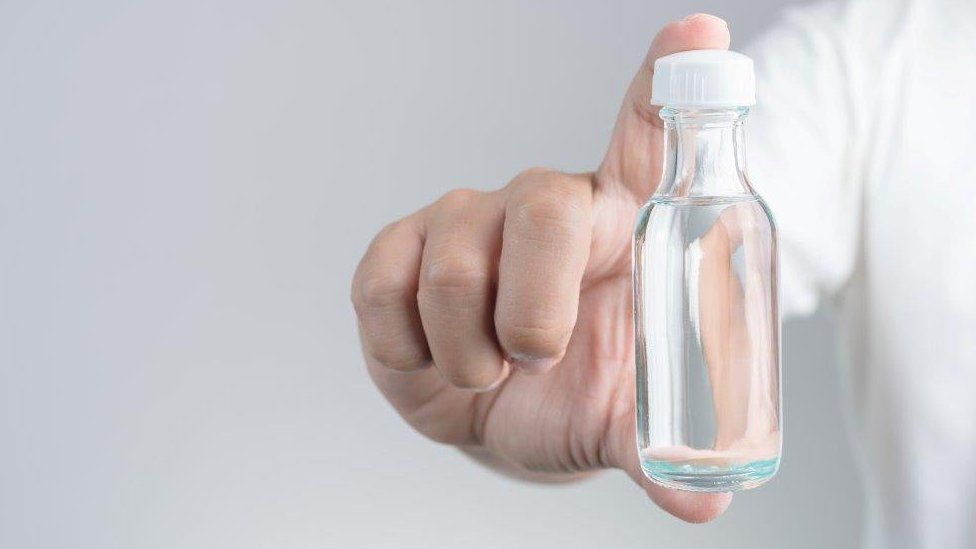 Hand with small bottle of clear liquid