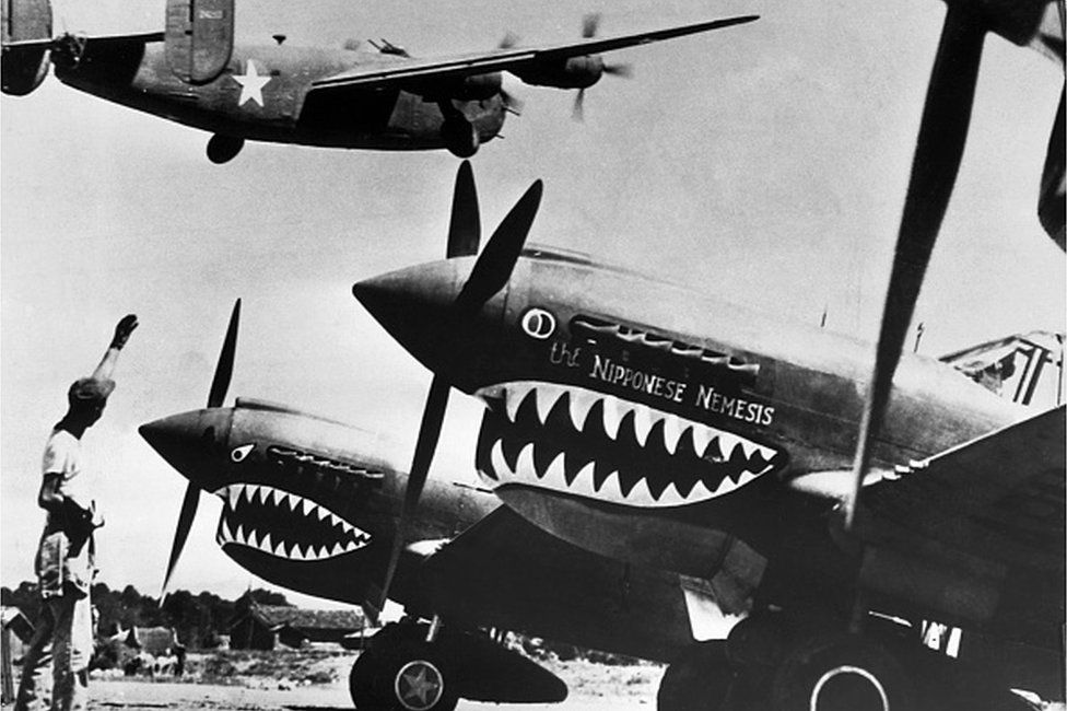 A bomber takes off for Japan above rows of Curtiss P-40 fighter planes painted with shark's teeth at a U.S. base in China.