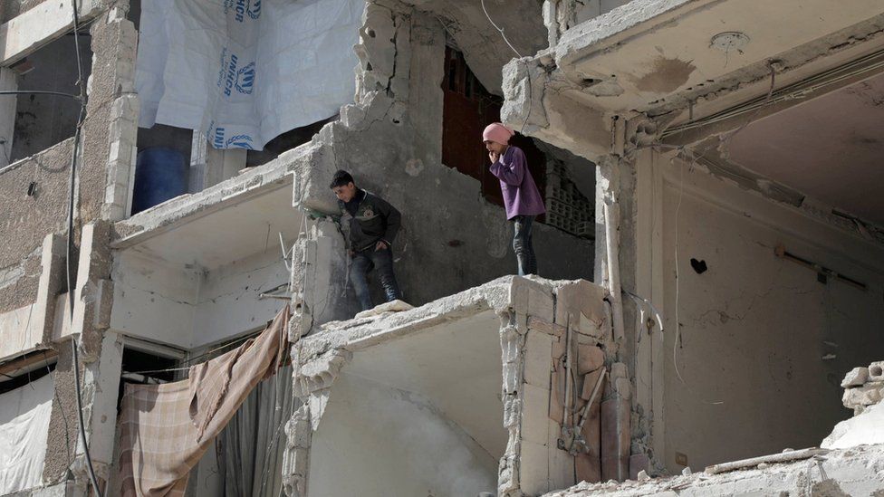 Syrian children look down from a destroyed building following air strikes on the rebel-held town of Douma, in the Eastern Ghouta (25 March 2018)