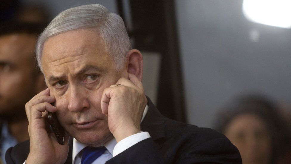 Benjamin Netenyahu puts a figner in his ear while listening intently to a phone call