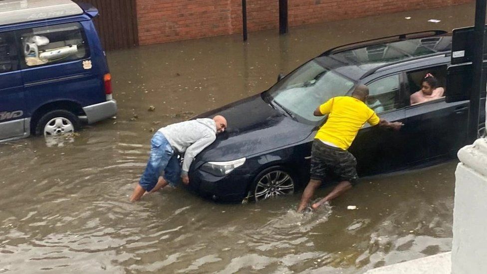 Neighbours help move a waterlogged car in Walthamstow in 2021