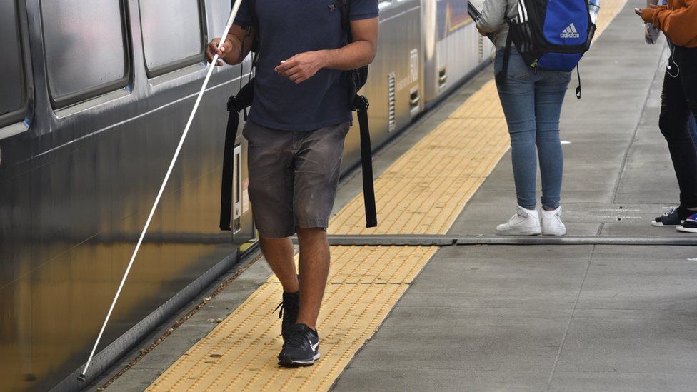 Visually impaired person with a stick next to a train