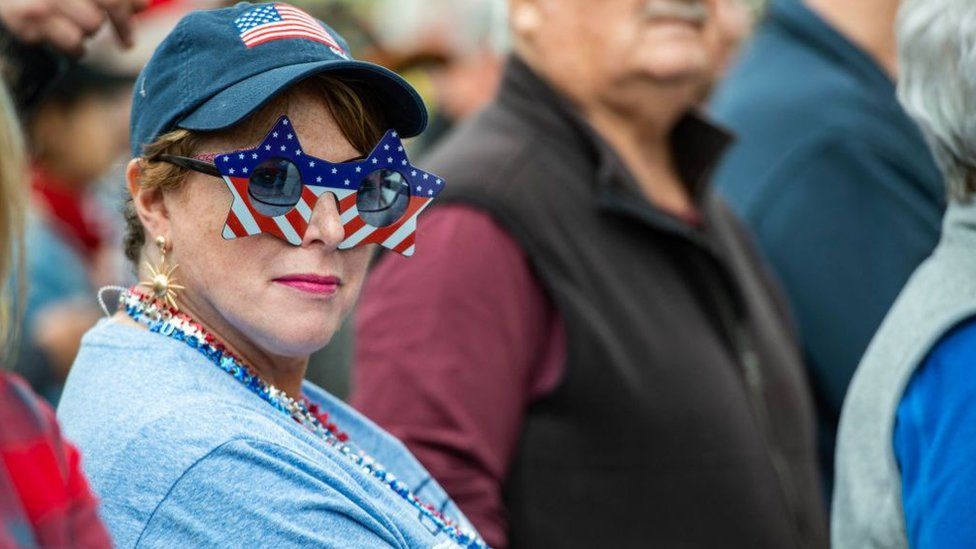Человек в очках с флагом США на митинге Трампа в Нью-Гэмпшире