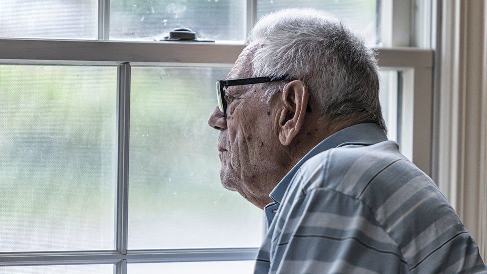 An elderly man look out of the window