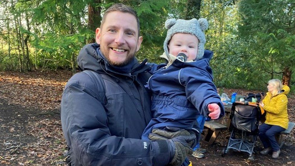 Adam holding his son Wilf in a woodland