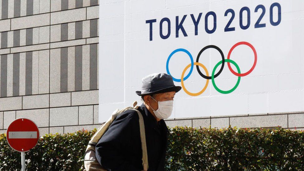A pedestrian wearing a face mask as a precaution against the Covid-19 coronavirus walks by a signage advertising the Tokyo 2020 Olympic Games in Tokyo.