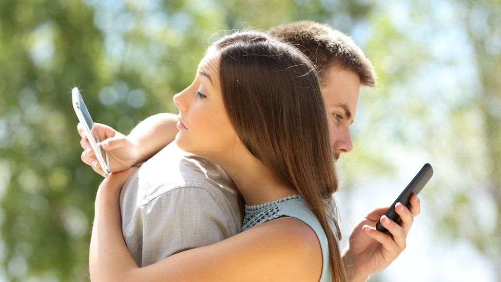 A couple hugging while on their phones