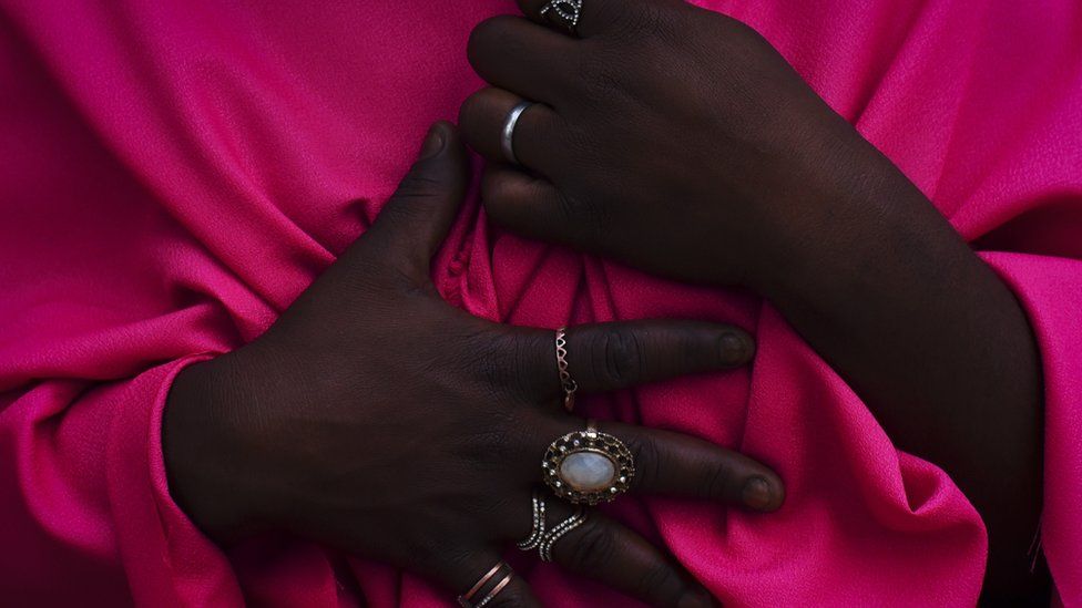 A woman's two hands with several rings, holding a pink garment.