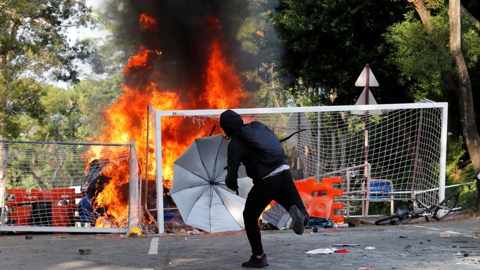 A university students throws an object at riot police