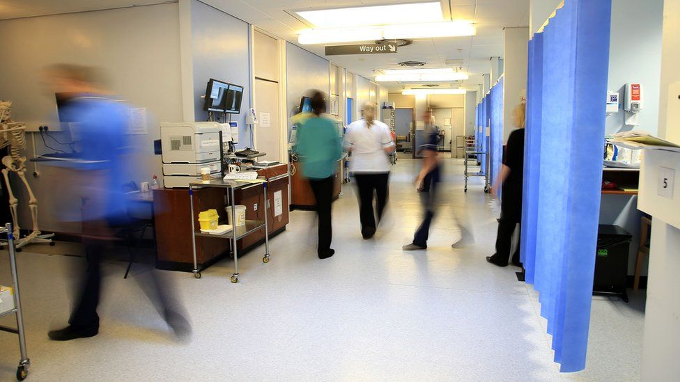 Nurses and other hospital staff are walking around a hospital ward.