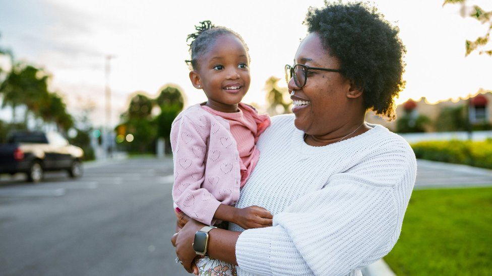 Woman holds daughter while walking outside