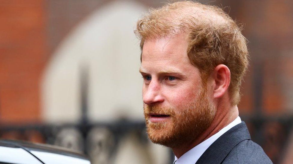 A close-up short of Prince Harry besides a car