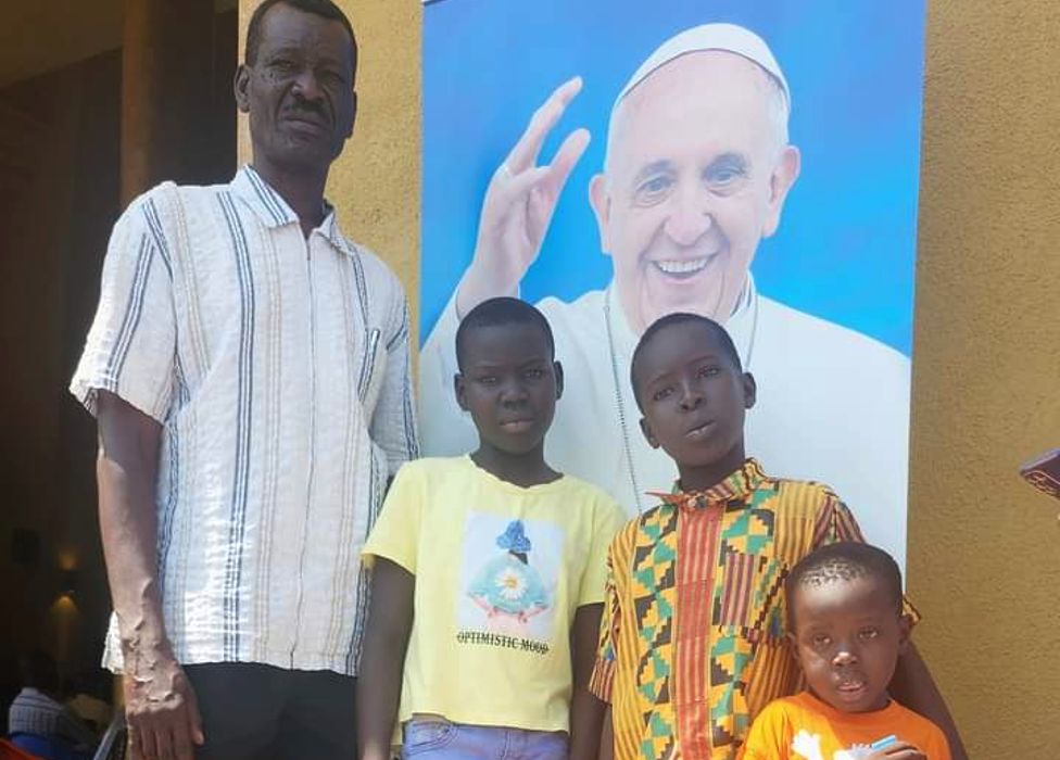 Lino Nyaro Ungom (L), a former teacher and activist in Juba, South Sudan, standing with children in front of a poster of the Pope