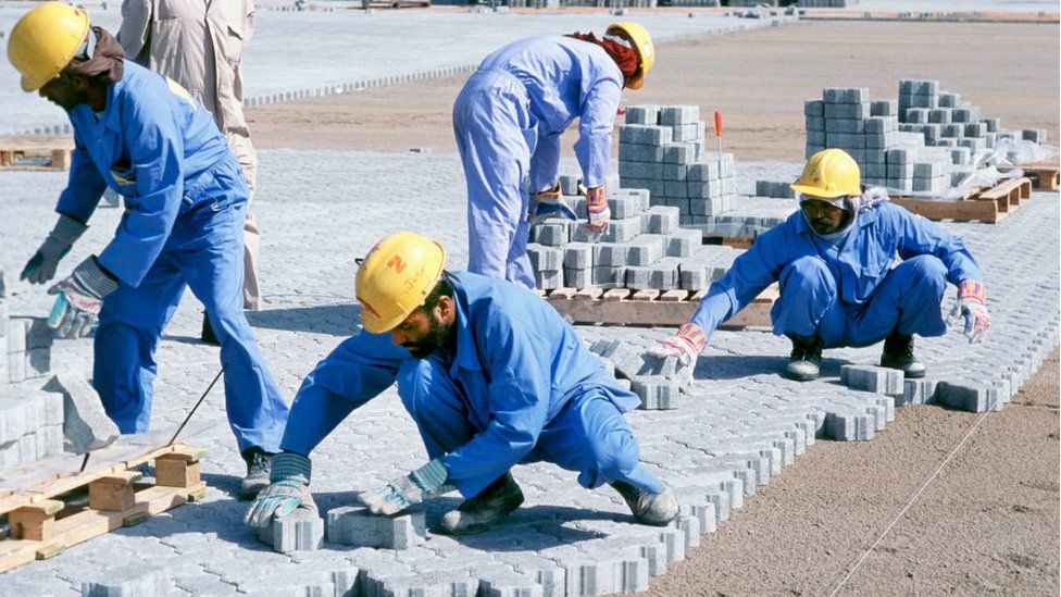 Construction workers laying block paving for container stacking areas, Dubai port Jebel Ali, UAE.