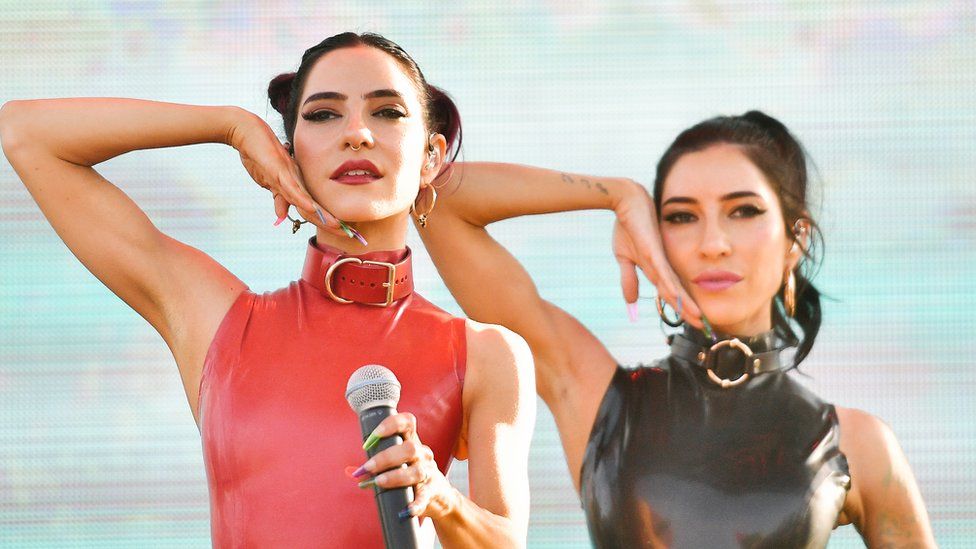 The Veronicas pose with one hand raised next to their cheeks in a performance in Los Angeles in 2019