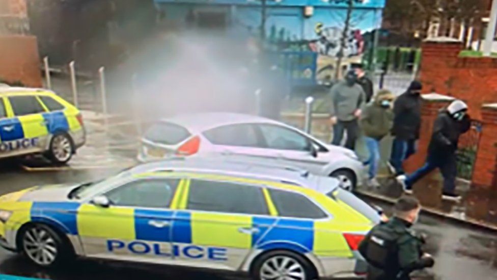 Masked men walk past police cars at Pitt Park in east Belfast on 2 February