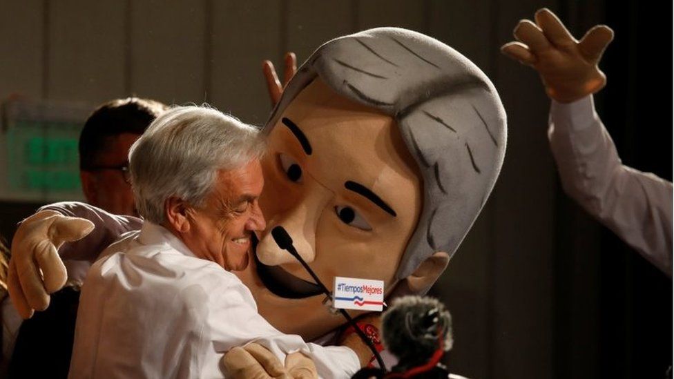 Кандидат в президенты Чили Себастьян Пинера (слева) обнимает человека в маске, изображающей его, во время собрания со сторонниками после лидерства в первом туре всеобщих выборов в Сантьяго, Чили 19 ноября 2017 г.
