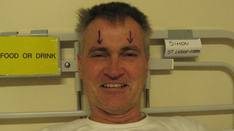 Man in hospital bed with two arrows drawn on above his eyes