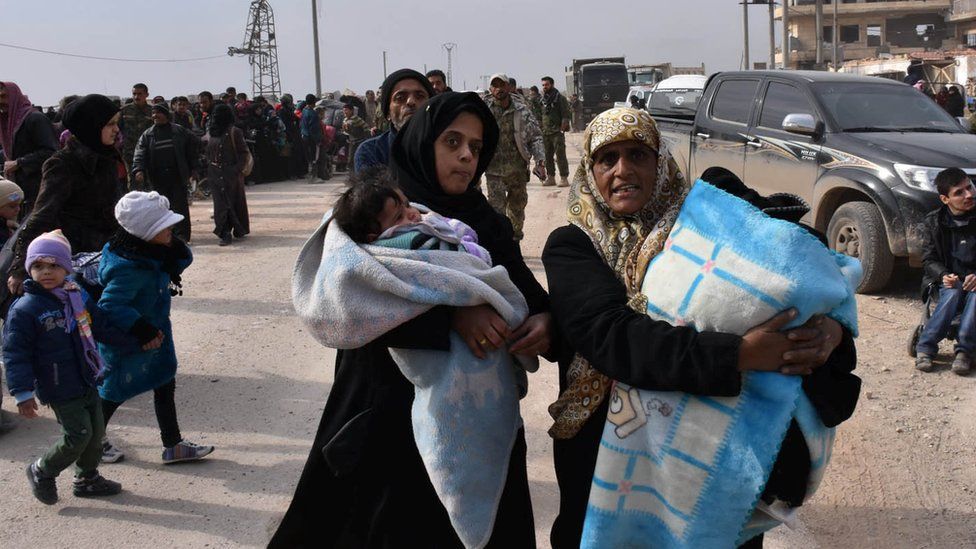 Two women clutch their belongings as they leave eastern Aleppo