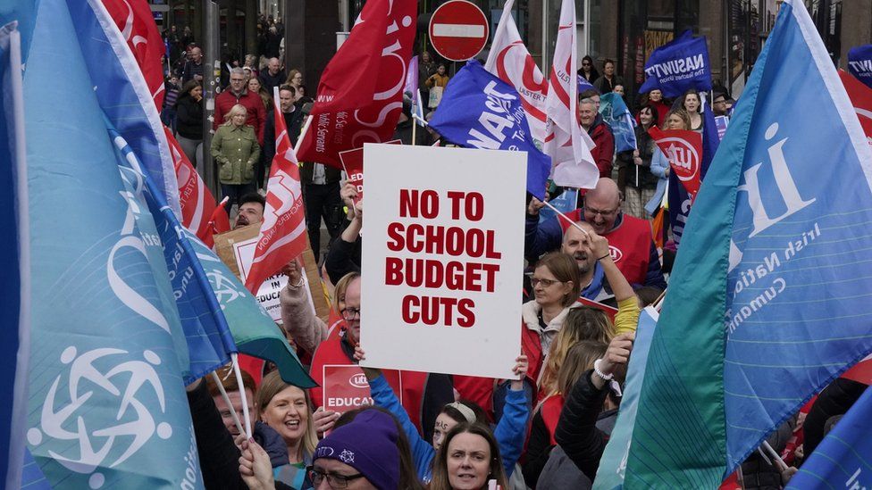 People hold up flags and placards in a rally against cuts in Belfast