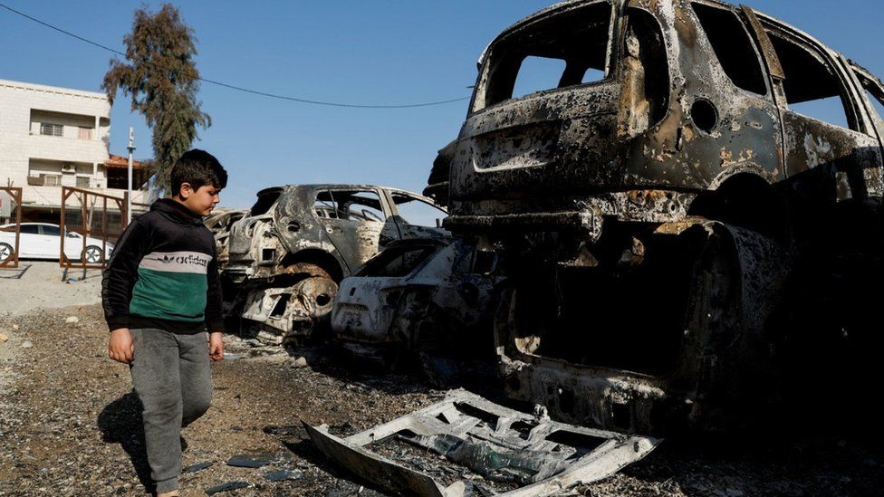 A Palestinian child walks near cars burnt near Hawara