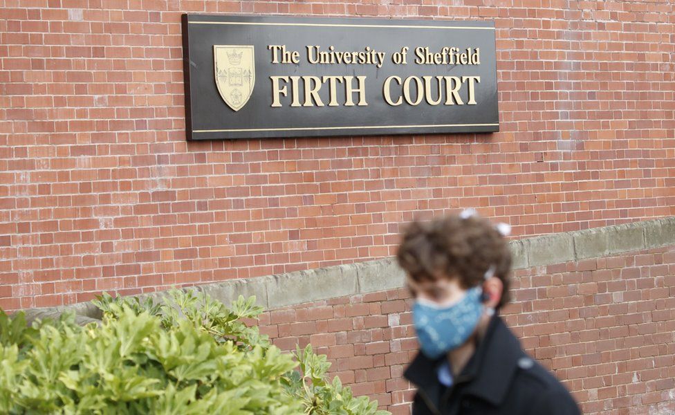 Man in facemask walks past University of Sheffield sign
