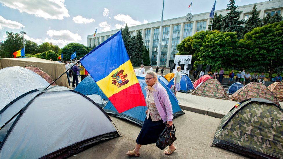 An elderly woman passes tents in front of a government building in Moldova