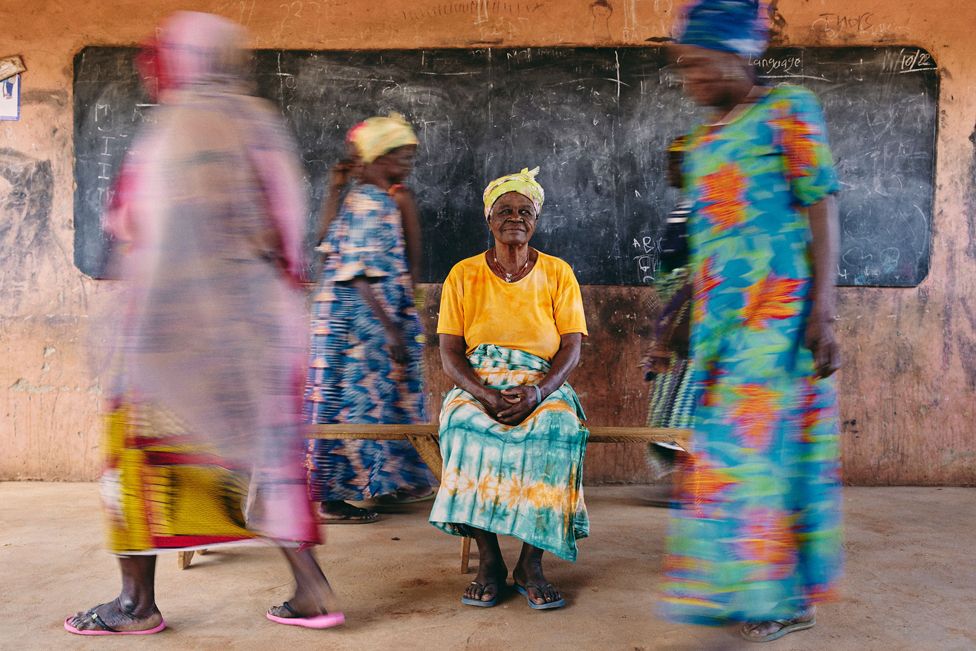 Сугри Зенабу, мангазия (женщина-лидер общины) «лагеря ведьм» Гамбага, сидит в окружении жителей в Гамбаге, Гана, 27 октября 2022 г.
