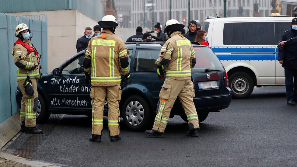Firefighters work near a car which crashed into the gate of the main entrance of the chancellery in Berlin