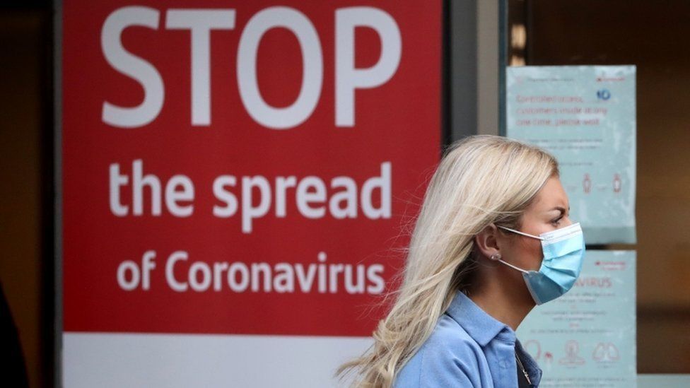 A woman wears a face mask and a sign says 'stop the spread of coronavirus'