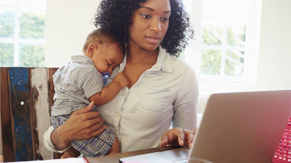 Woman on a laptop holding a baby