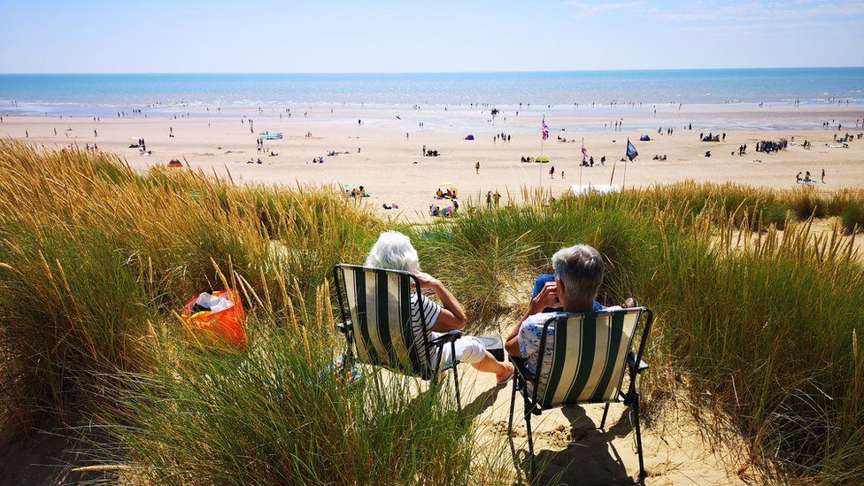 People sitting on deck chairs, enjoying the warm summer weather at Camber, East Sussex