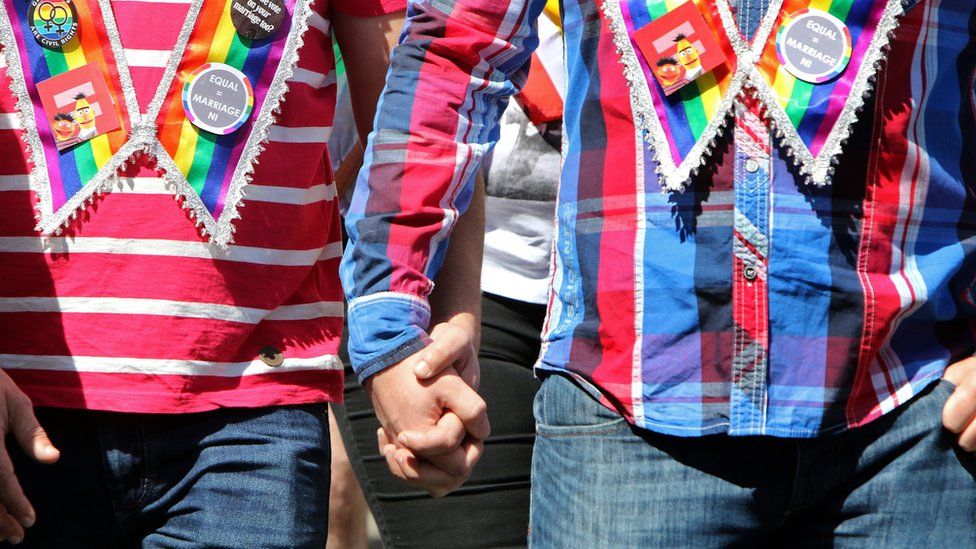 A couple hold hands as thousands of people walk through Belfast city centre to city hall, at a rally for gay marriage rights