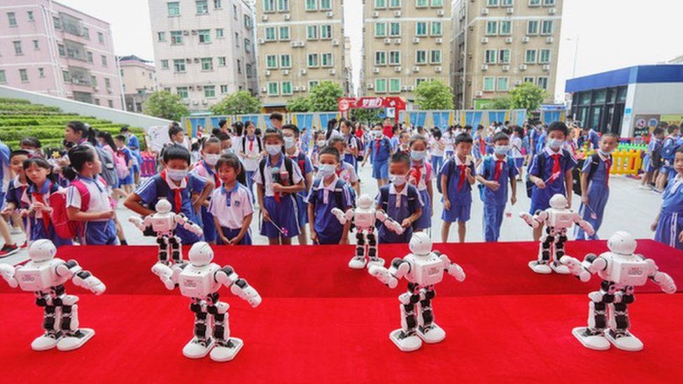 Little Nao robots lined up in front of schoolchildren