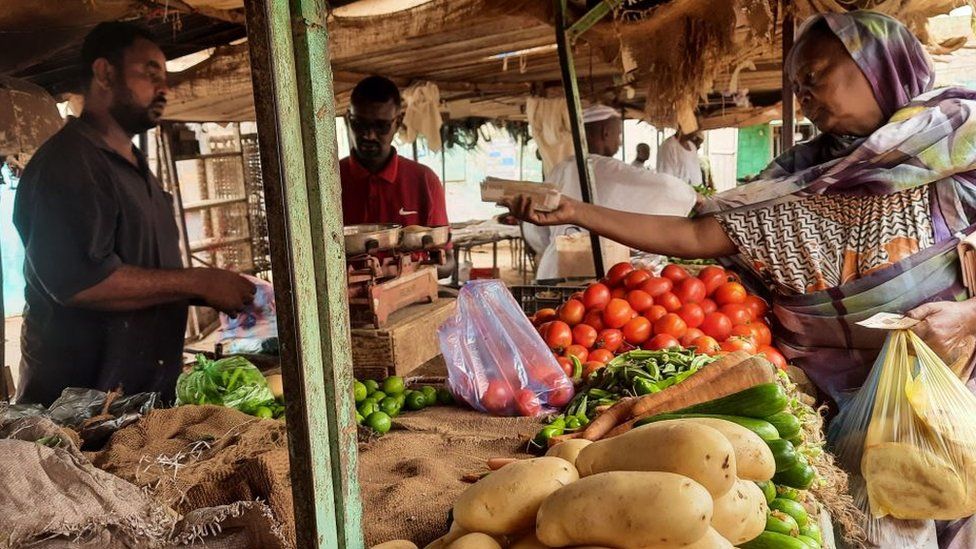 A woman buys fresh groceries from a market stall.