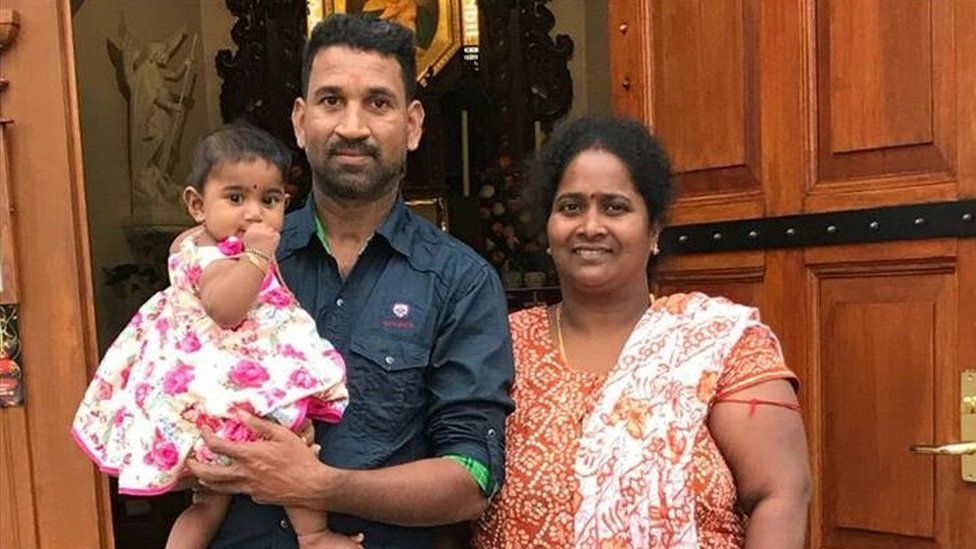 A family picture of Nadesalingam and Priya and their two daughters outside a door.