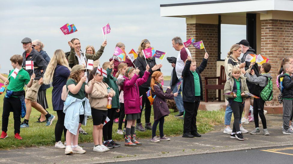 Onlookers wave flags at Whitley Bay