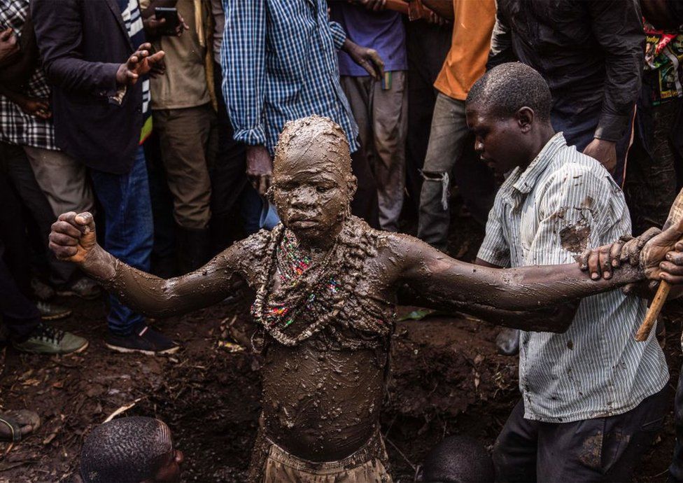 A boy covered in mud with his arms stretched out wide.