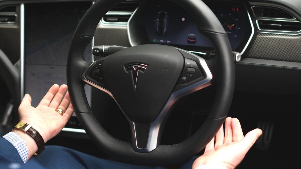 A driver takes their hands off a Tesla-brand wheel in the car